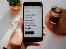 Hand hält Smartphone mit Text zur Markenkommunikation, daneben Kaffee, symbolisiert Brandvoice