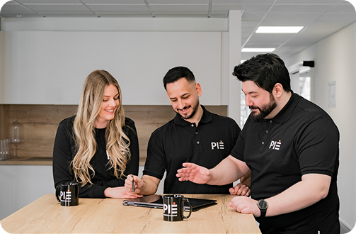 Drei PIE Marketing Agentur Mitarbeiter im Austausch am Tisch mit Laptop und PIE-Tassen