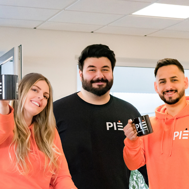PIE Marketing Teammitglieder mit PIE-Tassen und orangenen Hoodies, Jobseite